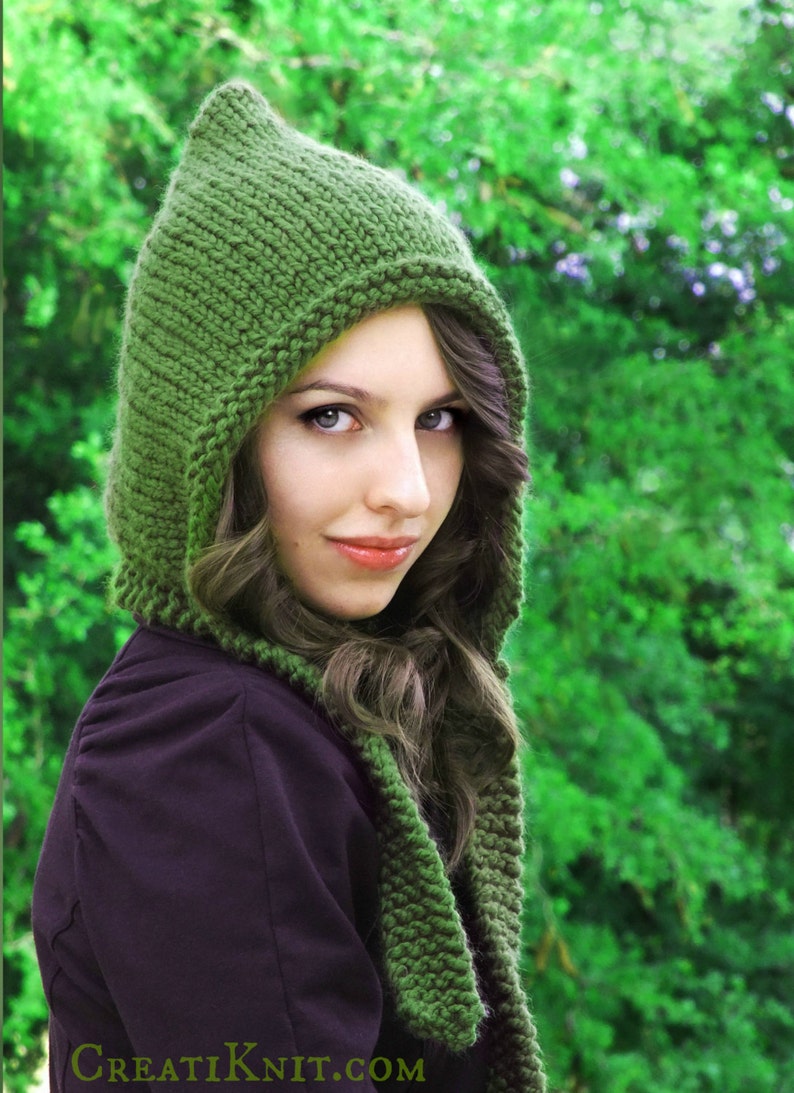 May include: A woman wearing a green knitted hooded scarf with a pointed tip. The scarf is made of a soft, chunky yarn and has a simple, elegant design.