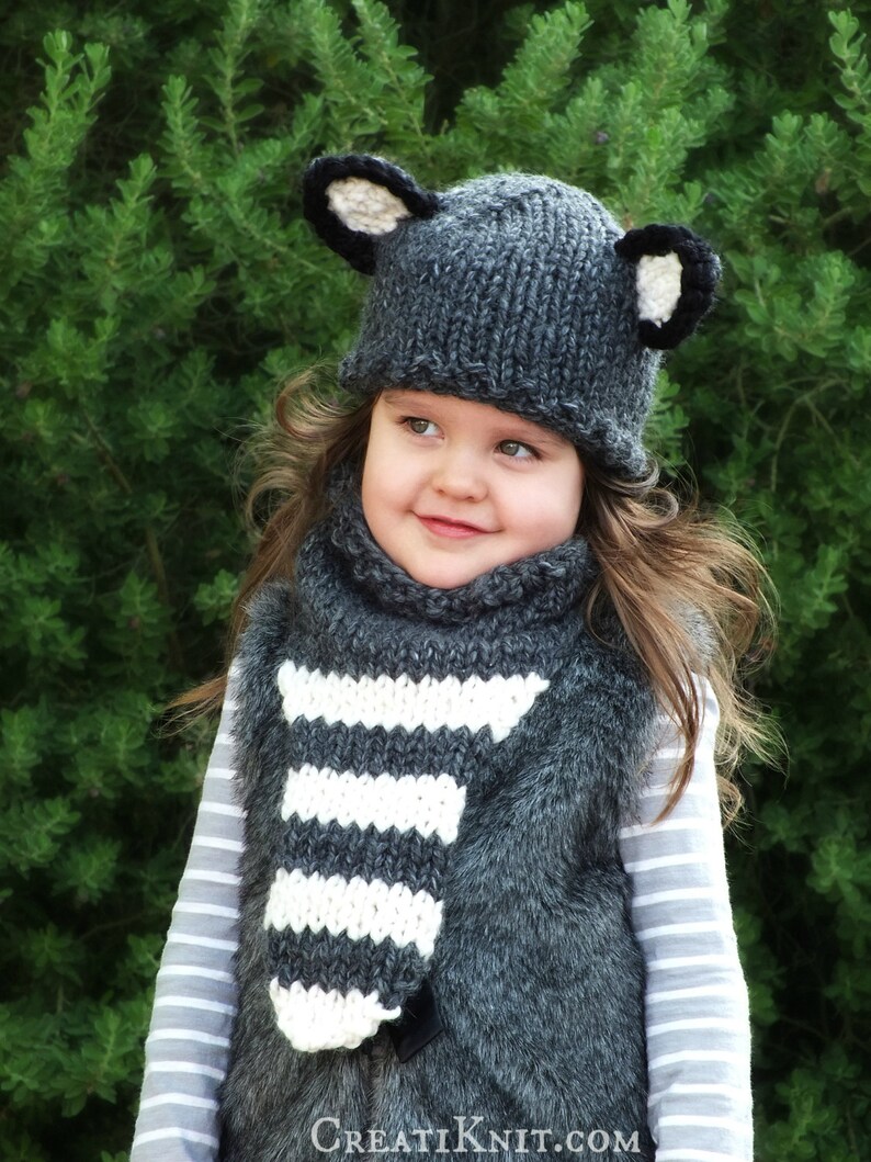 May include: A gray knitted hat with black ears and a white and gray striped scarf. The hat and scarf are worn by a child.