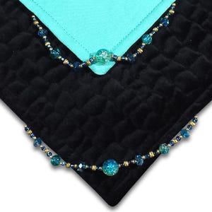 May include: Black quilted fabric with a turquoise accent. The fabric is adorned with beaded embellishments in shades of blue and gold. The beads are arranged in a decorative pattern, adding a touch of elegance to the design.