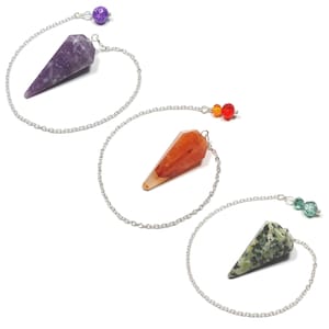 May include: Three crystal pendulums with silver chains and decorative beads. The crystals are purple, orange, and green with various patterns. The pendulums are used for divination and spiritual practices.