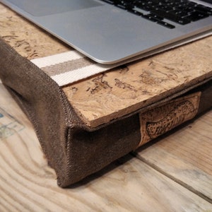 May include: A brown canvas laptop stand with a cork top and a white and brown striped fabric trim. The stand has a brown leather patch with the word "Forest" embossed on it.