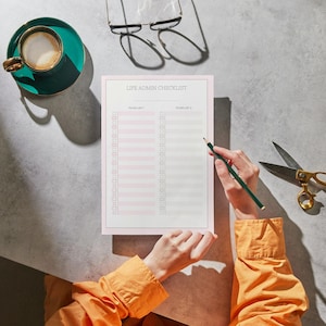 May include: A workspace scene featuring a notepad with "LIFE ADMIN CHECKLIST" text, a teal coffee cup, gold scissors, and a pencil. The notepad has pink accents. A person is writing on the notepad with a pencil.