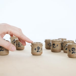 May include: A white ceramic mug with a black handle and the text "But First, Coffee" in a bold, black font. The mug is set against a blurred background, suggesting a cozy setting.