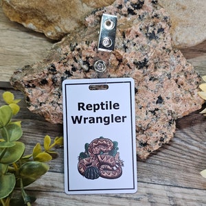 Puede incluir: Tarjeta blanca con el texto "Reptile Wrangler" y una imagen de dibujos animados de una serpiente de cascabel en un entorno desértico.