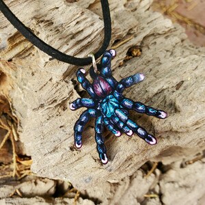 May include: A colorful tarantula pendant necklace. The pendant features a detailed illustration of a tarantula in shades of blue, purple, and teal. The necklace has a black cord.