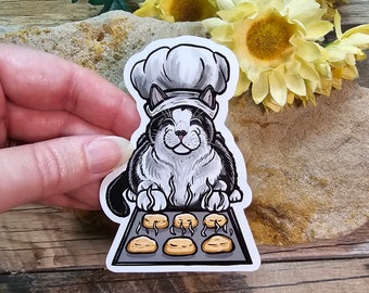 May include: A black and white cat wearing a white chef's hat bakes cookies on a baking sheet. The cat is smiling and has a happy expression. The cookies are golden brown and have steam rising from them.