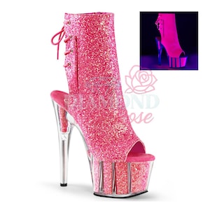 May include: Pink glitter open-toe ankle boots with a clear platform and heel. The boots have a lace-up back and a peep-toe design. The platform heel is approximately 15 cm high.