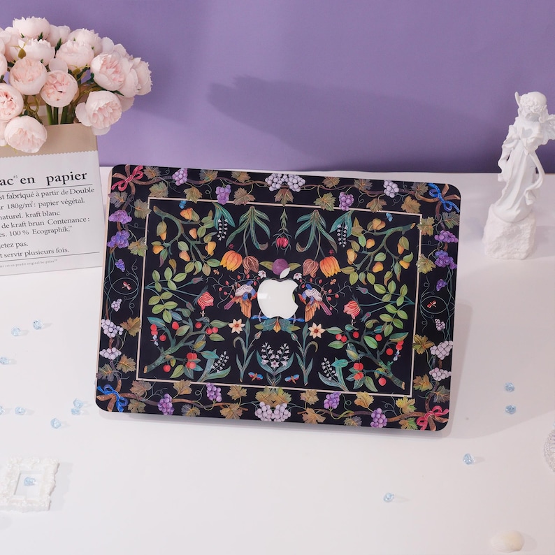 May include: A black laptop skin with a colorful floral design featuring birds and grapes. The design is intricate and detailed, with a variety of colors and patterns. The skin is made of a durable material and is designed to protect your laptop from scratches and wear.