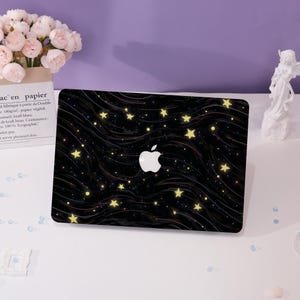 Op de afbeelding: Een zwarte laptop-skin met een sterrenhemelontwerp. De skin heeft een donkerblauwe achtergrond met witte sterren en een subtiel golfpatroon. Het Apple-logo is zichtbaar op de laptop.