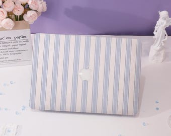Może przedstawiać: Biały laptop z niebiesko-białym wzorem w paski. Logo Apple jest widoczne na laptopie.