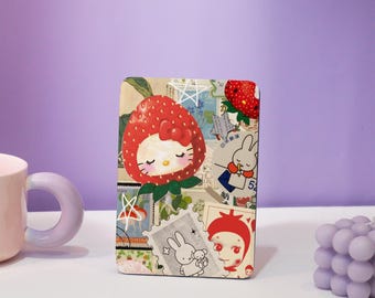 May include: A colorful collage featuring a cartoon strawberry with a Hello Kitty face, a bunny rabbit, and other whimsical designs. The collage is printed on a rectangular card.