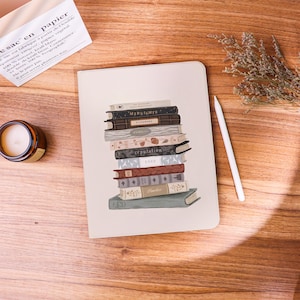 May include: A cream-coloured notebook featuring a central illustration of a vertical stack of ten books with various colours and titles including Midnights, Evermore, Reputation, and 1989. The notebook has rounded corners and a smooth, matte finish.