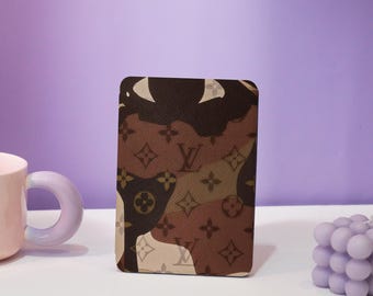 May include: A brown and beige camouflage pattern card holder with the Louis Vuitton logo.
