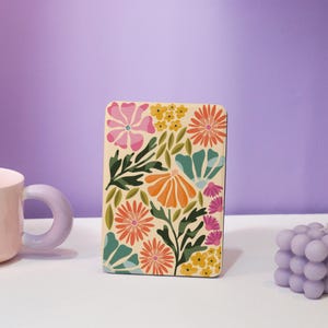 Puede incluir: Un diseño floral colorido impreso sobre un fondo crema. El diseño presenta flores y hojas rosas, naranjas, amarillas, verdes y azules.