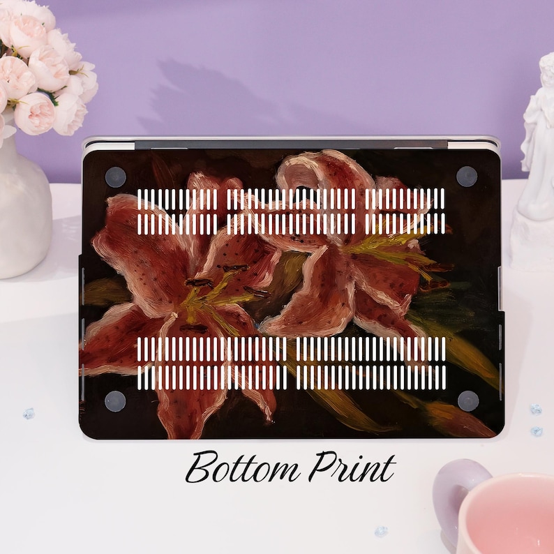 Peut inclure: Une coque d'ordinateur portable avec un imprim&eacute; floral repr&eacute;sentant des lys roses sur un fond sombre. La coque porte l'&eacute;tiquette "Bottom Print".