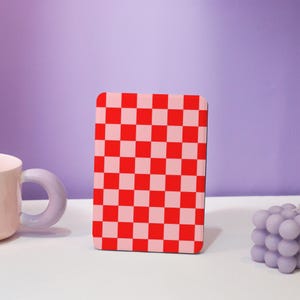 Può includere: Una custodia per telefono con un motivo a scacchi rosso e rosa. La custodia è realizzata in plastica rigida e ha una finitura liscia.