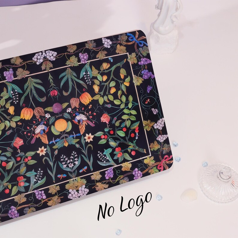 May include: A black rectangular placemat with a colorful floral design featuring birds, grapes, and flowers. The design is framed by a black border with a grapevine pattern.