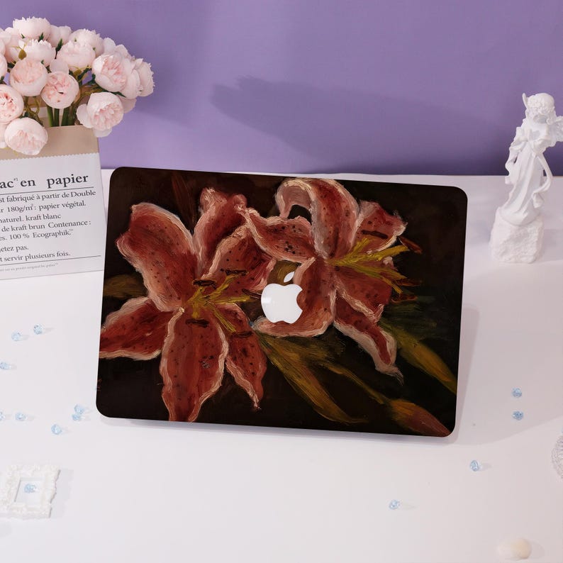 Peut inclure: Une peau d'ordinateur portable avec un motif peint de deux lys rouges sur un fond sombre. Le logo Apple est visible sur l'ordinateur portable.