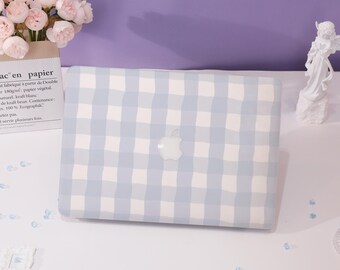 Może przedstawiać: Etui na laptopa w jasnoniebieską i białą kratę vichy z logo Apple. Etui leży na białej powierzchni. Bukiet różowych kwiatów i biała statua w tle.