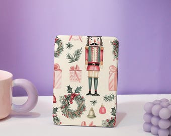 May include: A rectangular case with a festive Christmas pattern featuring a nutcracker, gifts, wreaths, bells, and ornaments. The design is set against a cream background with a purple backdrop.