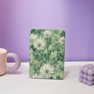 May include: A rectangular floral design featuring white daisies and green foliage. The design is set against a light green background, creating a soft, natural aesthetic. The image is of a decorative item, possibly a coaster or a small tray.