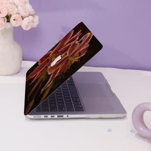 Peut inclure: Un ordinateur portable avec un motif floral sur le couvercle. Le motif repr&eacute;sente un gros plan d'une fleur rouge sur un fond sombre.