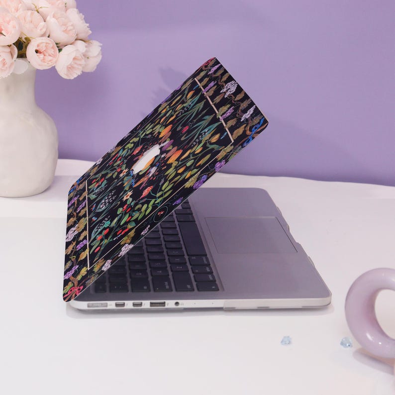 May include: A laptop computer with a floral design on the lid. The laptop is open and the screen is facing away from the viewer. The laptop is on a white surface.