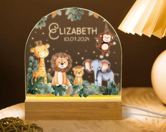 May include: A wooden night light with a clear acrylic insert featuring a jungle scene with a giraffe, lion, elephant, monkey, and a small lion cub. The acrylic insert is illuminated with a warm white light. The night light is personalized with the name "Elizabeth" and the date "10.07.2024".