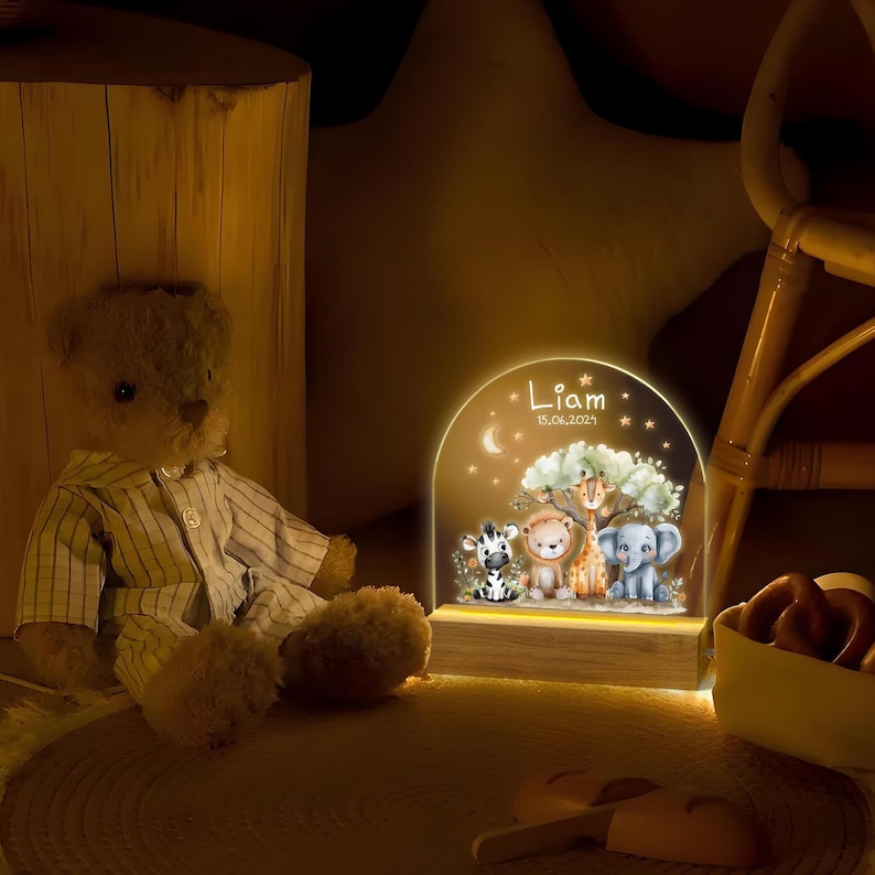 May include: A wooden night light with a clear acrylic insert featuring a whimsical illustration of a zebra, lion, giraffe, and elephant in a jungle setting. The light is personalized with the name "Liam" and the date "15.06.2021".