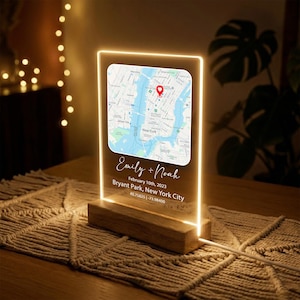 May include: A personalized LED light featuring a map of New York City with a red location marker. The light includes the names "Emily + Noah", the date "February 10th, 2023", and the location "Bryant Park, New York City". The light is set on a wooden base.