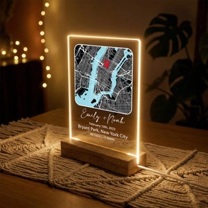 May include: A personalized LED light featuring a map of New York City with a red marker. The light includes the names "Emily + Noah", the date February 10th, 2023, and the location Bryant Park, New York City. The light is set on a wooden base.