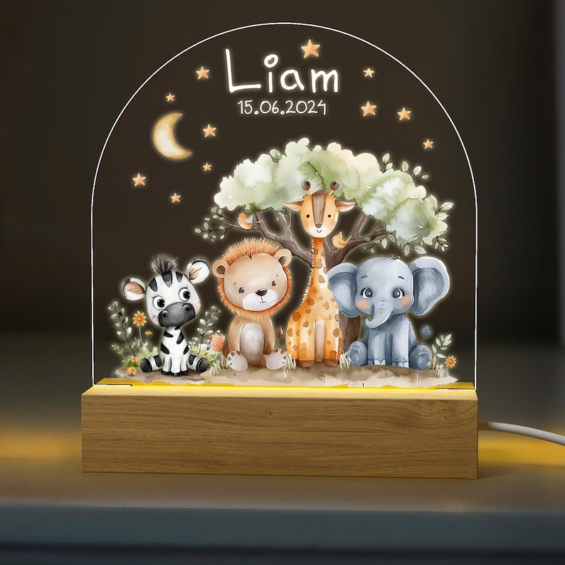 May include: A wooden night light with a clear acrylic insert featuring a whimsical jungle scene with a zebra, lion, giraffe, and elephant. The text "Liam 15.06.2021" is printed on the acrylic insert.