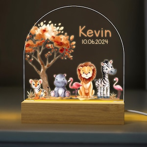 May include: A wooden night light with a clear acrylic panel featuring a jungle scene with a lion, zebra, hippopotamus, tiger, and flamingos. The panel also includes the name "Kevin" and the date "10.06.2024".