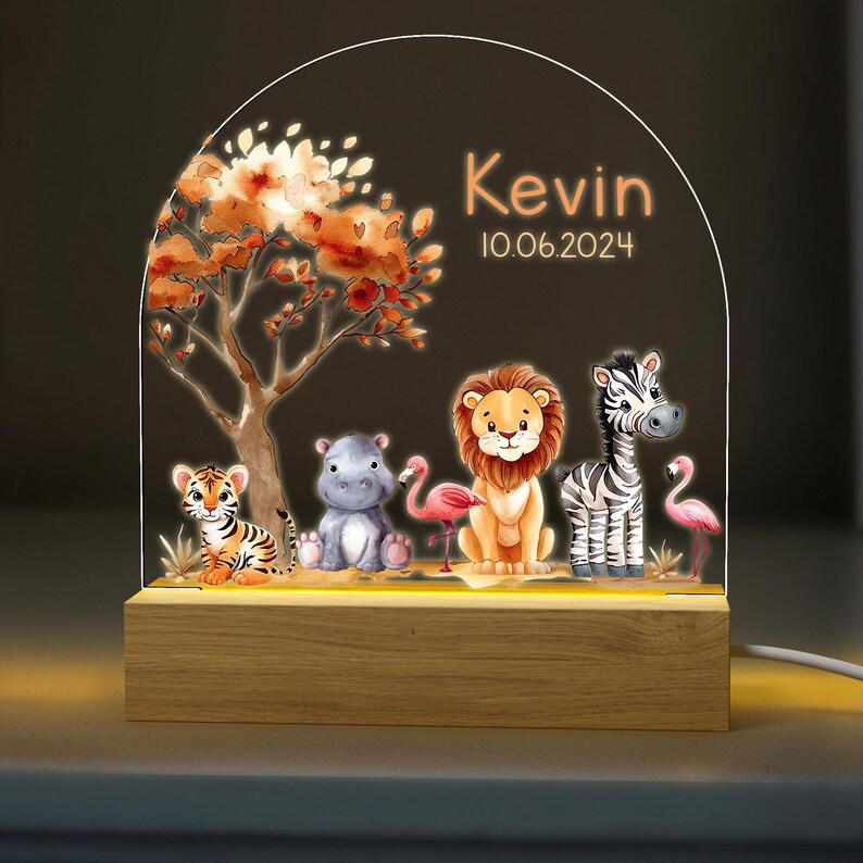May include: A wooden night light with a clear acrylic panel featuring a jungle scene with a lion, zebra, hippopotamus, tiger, and flamingos. The panel also includes the name "Kevin" and the date "10.06.2024".