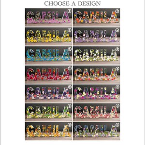 May include: A selection of decorative resin name signs spelling "CAMILA", each filled with colorful flowers. The signs are in various colors and floral arrangements, with the text "CHOOSE A DESIGN" at the top.