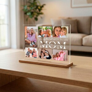 Pode incluir: Um expositor de fotos em acrílico transparente com base em madeira. O expositor apresenta várias fotos de família e o texto "You are the best mom in the world" e "MOM". O expositor é um presente sentimental.