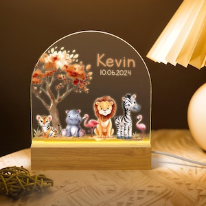 May include: A wooden night light shaped like an arch with a jungle scene. The scene includes a zebra, a hippopotamus, a lion, a flamingo, and a tiger. The night light is personalised with the name "Kevin" and the date "10.06.2024".