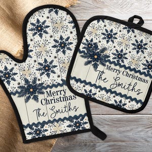 May include: A matching oven mitt and pot holder set. The set features a cream-colored background with a pattern of navy blue and cream-colored floral designs. The words "Merry Christmas The Smiths" are printed on both items.
