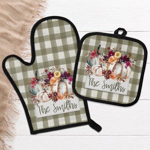 May include: An oven mitt and a square pot holder featuring a sage green and white buffalo check pattern. Both items display a printed graphic of pumpkins and autumn flowers with the text The Smiths written in a black cursive script font.