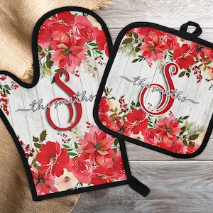 May include: A matching oven mitt and pot holder set featuring a floral design with red poinsettias and greenery on a white wood-look background. The set includes the name "the smiths" and a large red initial "S". The edges are trimmed in black.