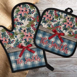 Könnte beinhalten: Ein passendes Ofenhandschuh- und Topflappen-Set. Der obere Teil zeigt ein Blumenmuster mit rosa Blüten, grünen Blättern und roten Beeren. Der untere Teil hat ein blaues Karomuster mit dem Namen "The Smiths" in roter Schrift, akzentuiert mit einer roten Schleife.