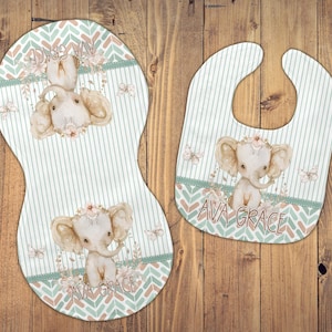 May include: A set of two baby bibs with a green and brown chevron pattern. The bibs feature a cute elephant illustration with a floral crown and the name "Ava Grace" printed on each bib.