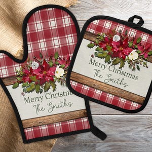 May include: A red and white plaid oven mitt and pot holder set. Both items feature a floral design with red poinsettias, white flowers, and green leaves. The text "Merry Christmas The Smiths" is displayed on both items.