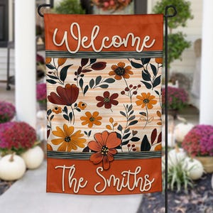 May include: A garden flag with a fall theme, featuring the word "Welcome" in white script at the top and "The Smiths" at the bottom. The flag has a floral design with orange, brown, and yellow flowers and foliage.
