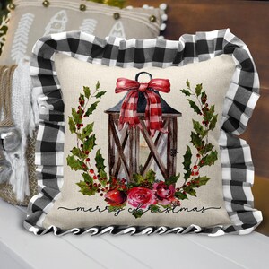 May include: A decorative Christmas pillow with a black and white buffalo check ruffle. The pillow features a watercolor design of a lantern, holly, and roses, with the words "merry christmas" in script.