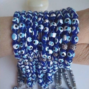 Peut inclure: Une pile de bracelets en perles bleues et blanches avec des breloques et des glands argent&eacute;s.