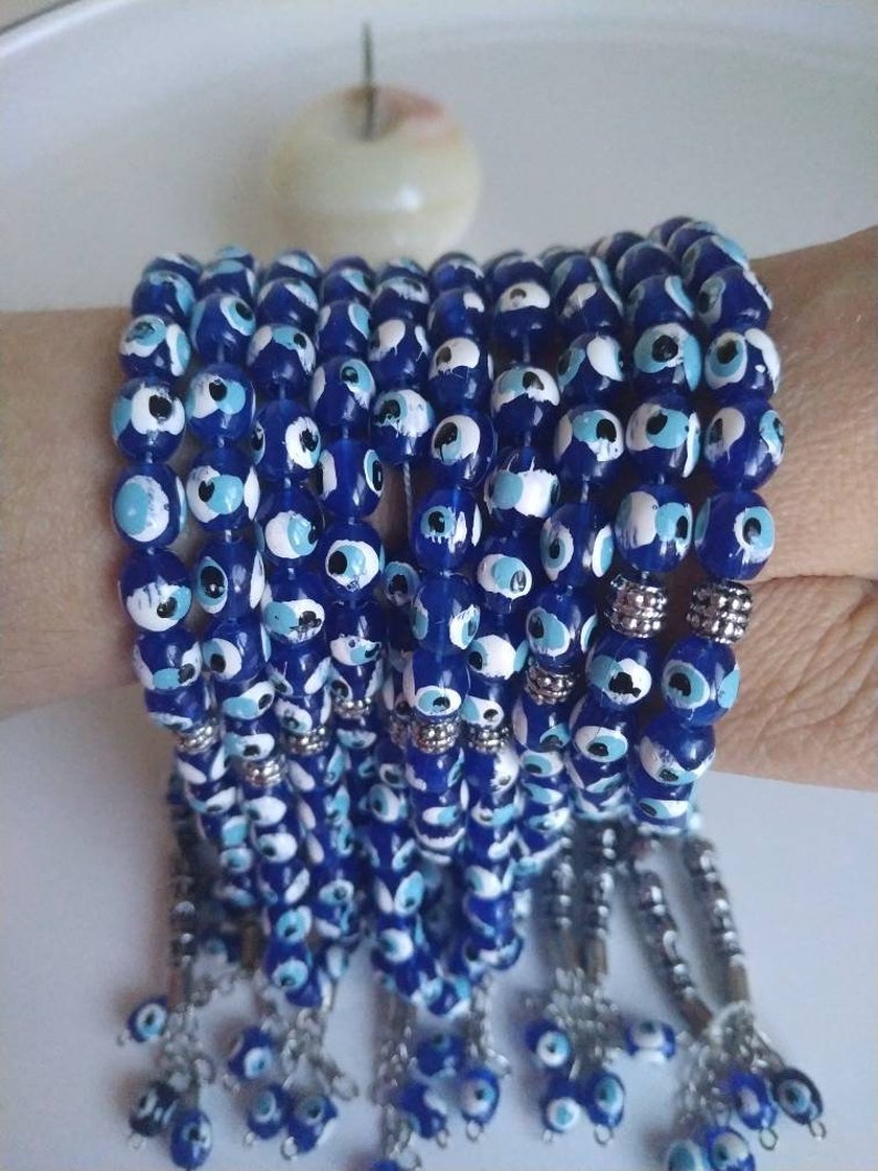 Peut inclure: Une pile de bracelets en perles bleues et blanches avec des breloques et des glands argent&eacute;s.