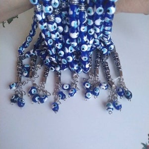 Peut inclure: Un ensemble de bracelets en perles bleues et blanches avec des breloques argent&eacute;es. Chaque bracelet a un pompon avec plusieurs perles en forme d'&oelig;il mal&eacute;fique.