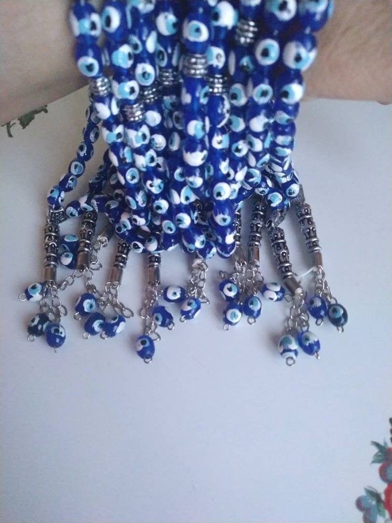 Peut inclure: Un ensemble de bracelets en perles bleues et blanches avec des breloques argent&eacute;es. Chaque bracelet a un pompon avec plusieurs perles en forme d'&oelig;il mal&eacute;fique.