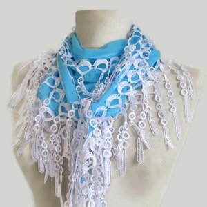 May include: A light blue scarf with a white lace trim and fringe detail. The scarf is draped over a mannequin, showcasing the delicate openwork design and the contrast between the colors. The scarf is a fashion accessory.